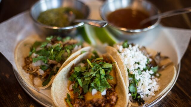 Three tacos topped with cilantro and crumbled cheese, served with two small bowls of salsa, at Native Tongues Taqueria in Calgary in June 2016.