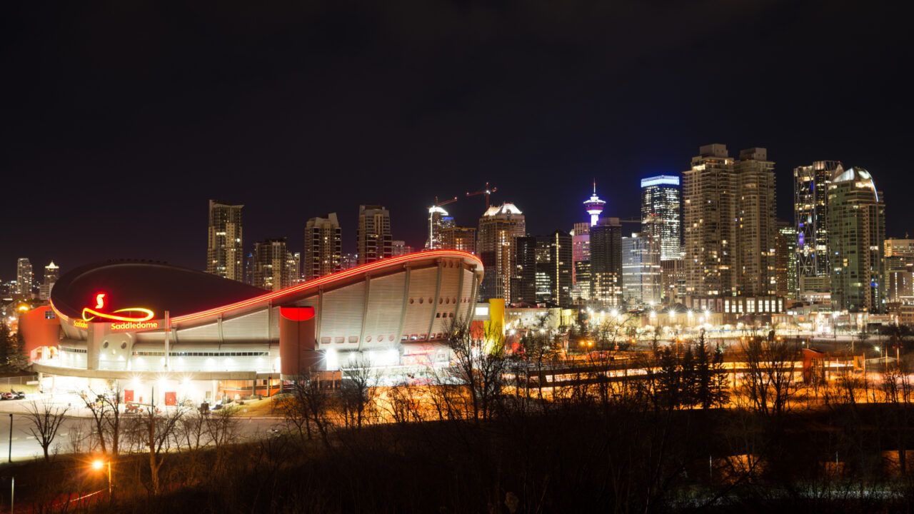 The Scotiabank Saddledome lit up at night with the downtown Calgary skyline behind it, photographed in April 2020.