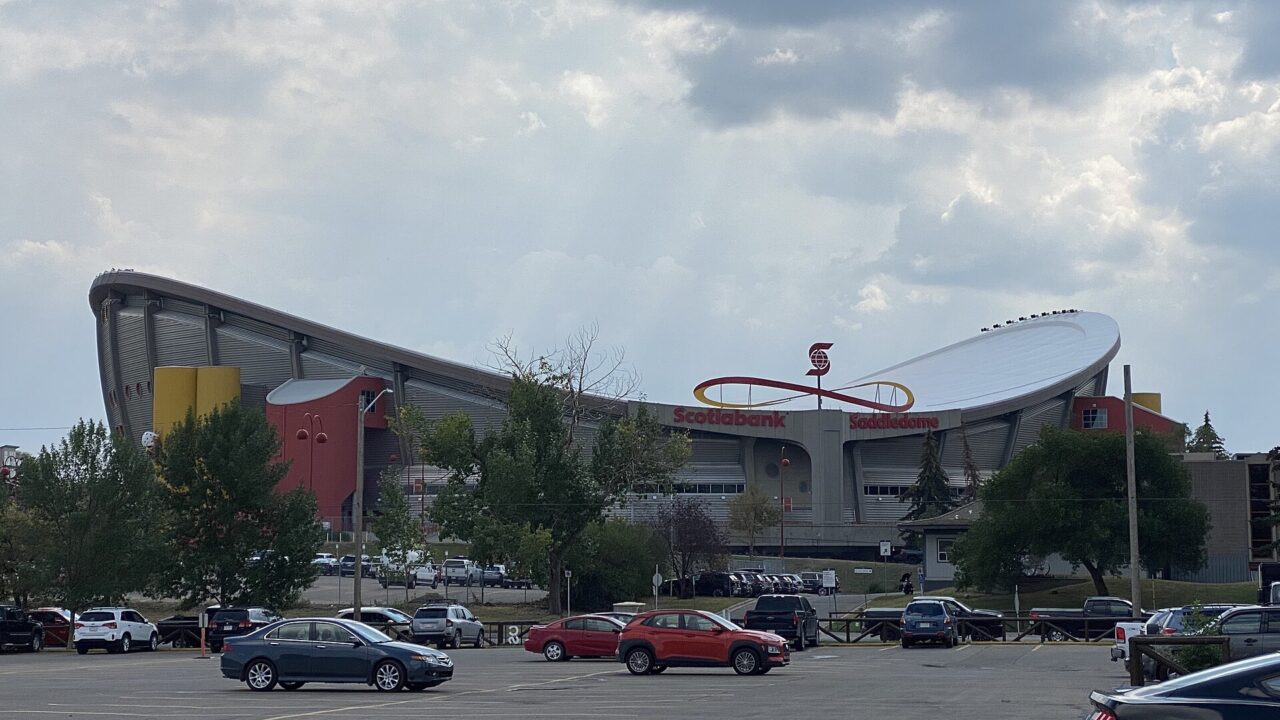 Cars parked in a Stampede Park surface lot with the Scotiabank Saddledome behind them, photographed in August 2022.