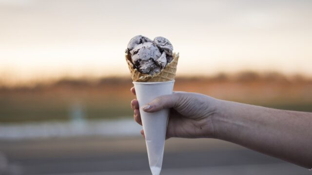 A hand holding an ice cream in a waffle cone; an illustration, not taken at Village Ice Cream.